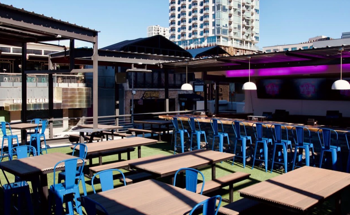 Willow's rooftop in daylight with picnic tables, green turf, a pergola and a downtown Austin tower behind