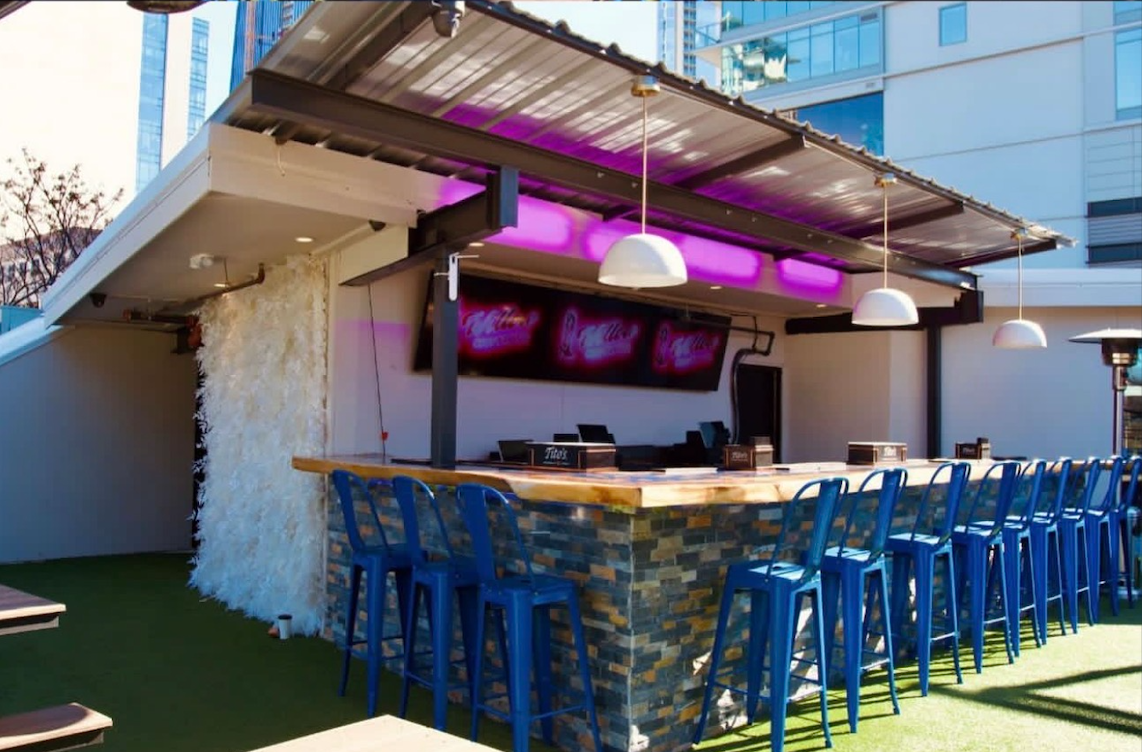 Willow's rooftop bar in daylight with a live-edge wood top, stone base, bar stools and neon Willow screens