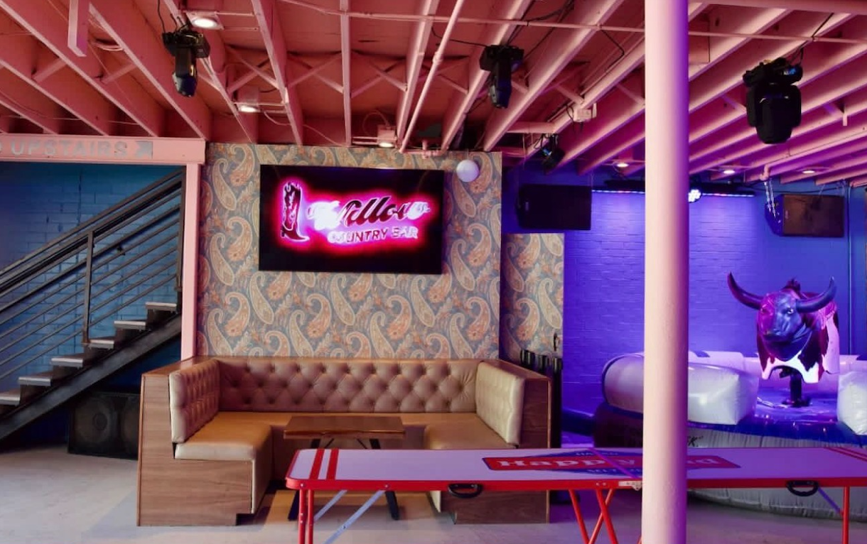 Willow's downstairs room with a tufted leather booth, neon Willow boot sign on paisley wallpaper and the mechanical bull at right